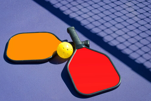 2 Pickleball paddles and a pickleball laying on pickleball court at Corpus Christi Athletic Club